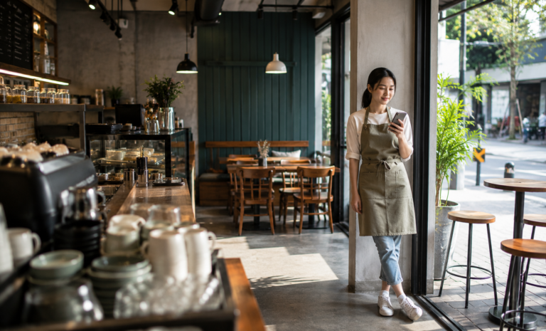 FEATURED IMAGE "A high-resolution photoreal photograph of a Chinese female cafe owner in her early 30s glancing at the day's sales summary on a phone, standing at a quiet corner of her cafe just after the morning rush has cleared. Set in a modern Singapore neighbourhood cafe, warm natural light through the shopfront window, a few cups on the counter softly out of focus in the foreground. Wide establishing shot, slightly elevated, deep focus showing the whole space. The owner appears calm, satisfied, forward-looking. Photoreal photography, not illustration, not 3D render. Bright natural daylight, premium magazine quality, clean and uncluttered scene. Aspect ratio close to 1200x728. No text overlay, no captions, no graphics, no logos. No stressed or melancholic expressions. No fake or distorted hands or text. No stock-photo cliche poses. No Western office settings." Alt text: Cafe owner reviewing daily sales on phone — Labamu POS Singapore IN-ARTICLE IMAGE (sekitar H2 #3: morning takeaway queue) "A high-resolution photoreal photograph of an Indian male barista in his late 20s completing a takeaway transaction at a sleek cafe counter, a customer tapping their phone to pay via QR. Over-the-shoulder shot framing what the customer sees at the counter, shallow depth of field. Set in a busy Singapore cafe during morning peak hours, warm overhead lighting, a short queue softly visible in the background. The barista appears focused, efficient, in-control. Photoreal photography, not illustration, not 3D render. Bright warm ambient lighting, premium magazine quality, clean and uncluttered. Aspect ratio close to 1200x728. No text overlay, no captions, no graphics, no logos. No stressed or overwhelmed expressions. No fake or distorted hands or text. No cluttered or messy environment. No Western office settings." Alt text: Barista processing takeaway payment at Singapore cafe counter during morning rush